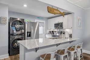 Una cocina moderna con una isla central, taburetes de bar, electrodomésticos de acero inoxidable y una decoración con forma de pez colgado.