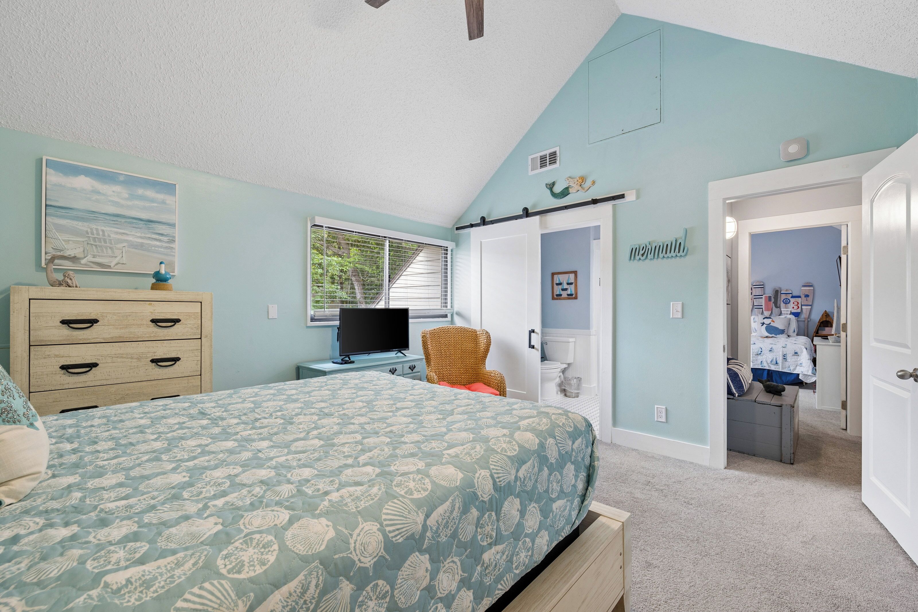 A bedroom with a bed, dresser, television, and a door leading to another room.