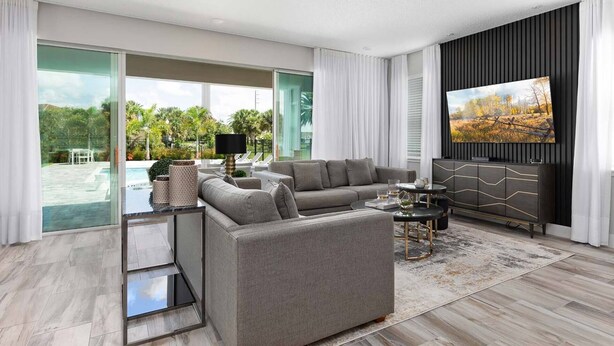 A modern living room with a grey sectional sofa, a glass coffee table, and a flat-screen TV mounted on a black panel wall. - The Perfect Villa with a beautiful Private Pool, Orlando Villa 5601 (Orlando)