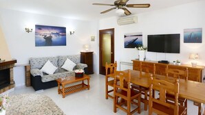 Ein Wohnzimmer mit Sofa, Couchtisch, Esstisch, Stühlen, Deckenventilator und Bildern an den Wänden.