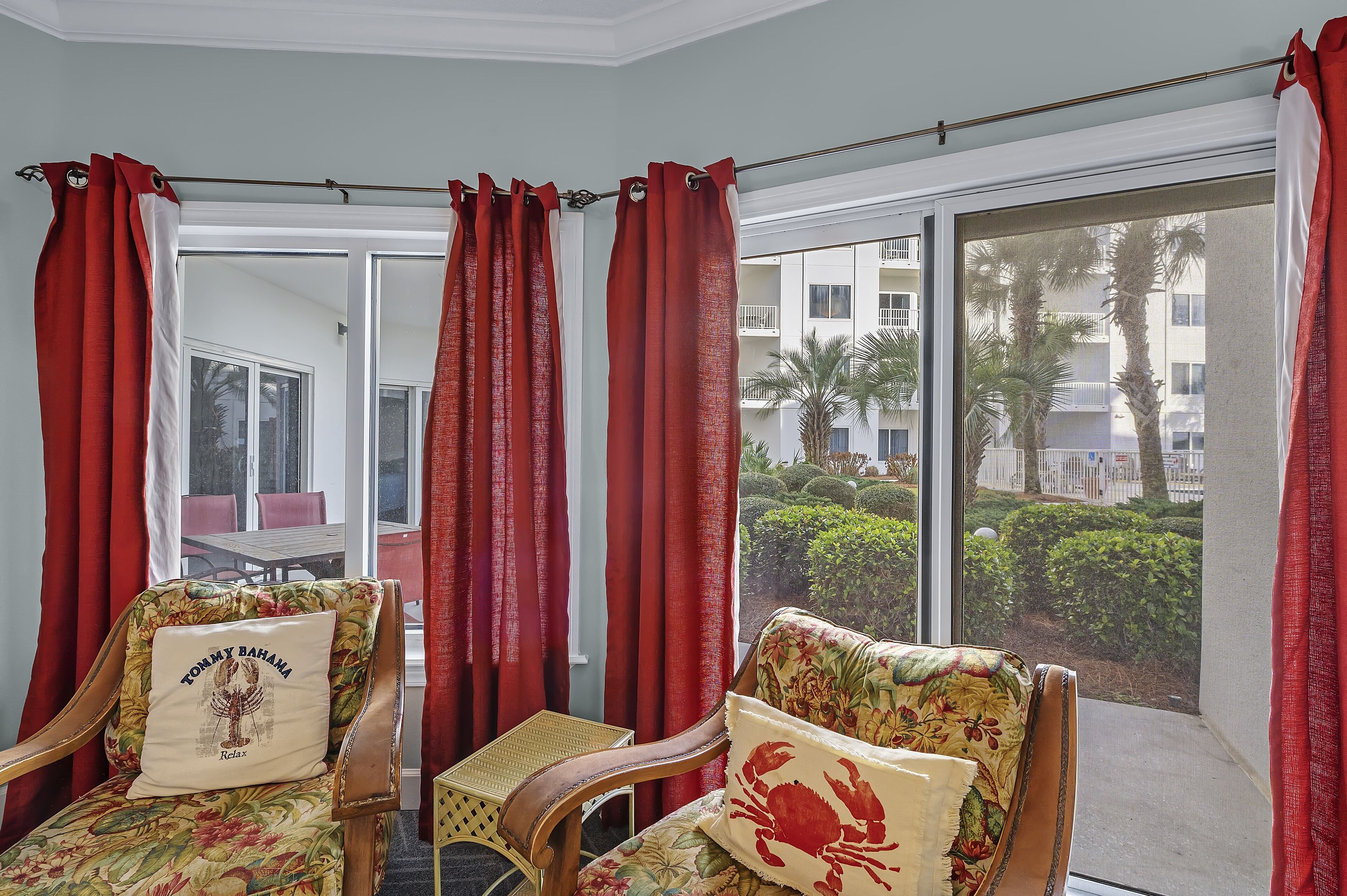 Una habitación con dos sillas de madera tapizadas con motivos florales, una mesita y cortinas rojas.