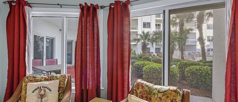 Una habitación con dos sillas de madera tapizadas con motivos florales, una mesita y cortinas rojas.