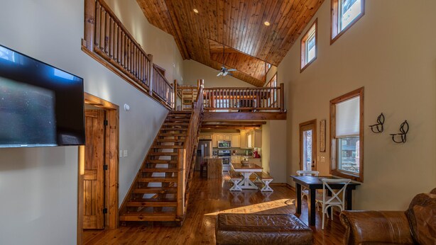 Un vaste espace de vie comprenant un escalier en bois menant à une mezzanine, un coin repas et une cuisine.
