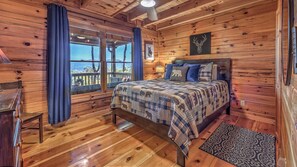 Une chambre dans une cabane en bois, avec un grand lit, une vue par la fenêtre et une commode en bois.