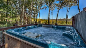 Un bain à remous avec une terrasse en bois et une vue sur les arbres et les collines.