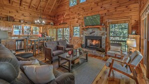 Interior acogedor de una cabaña con chimenea, paredes de madera, una zona de comedor y una sala de estar amoblada con sofás y una mesa de centro.