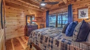Un dormitorio de cabaña de madera con cama, cómoda y una ventana grande con vistas.
