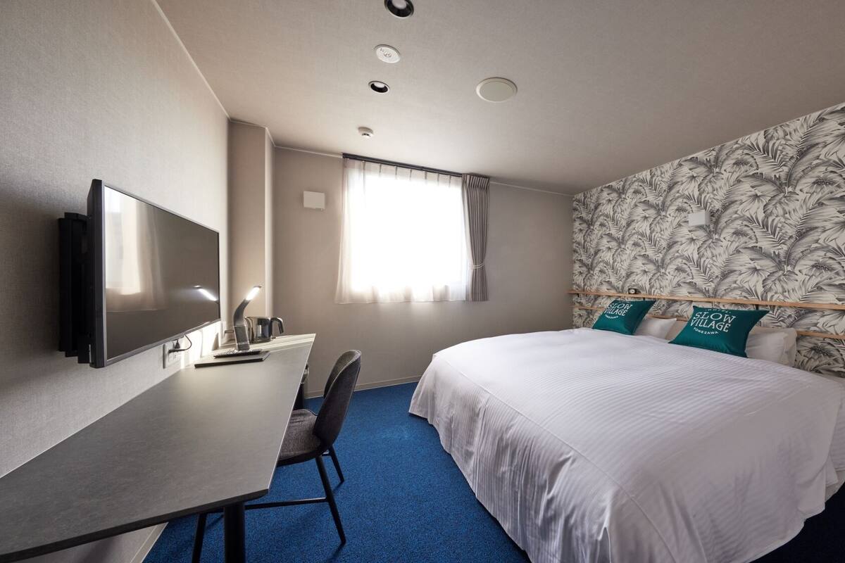 A hotel room with a bed, a desk, a chair, a TV, and a window with curtains.
