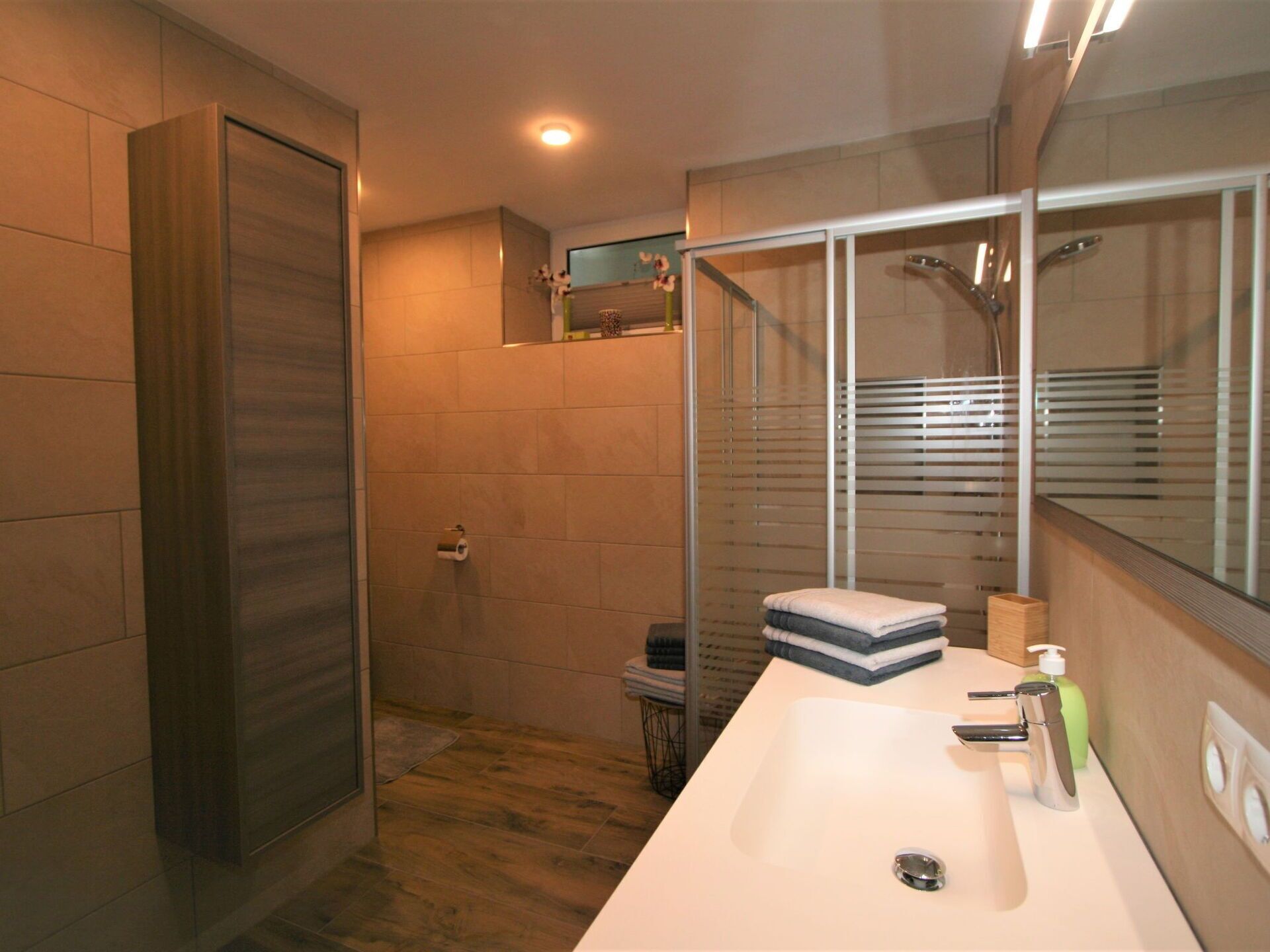A modern bathroom with a large mirror, a shower enclosure, and a white sink.