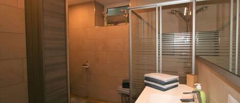 A modern bathroom with a large mirror, a shower enclosure, and a white sink.