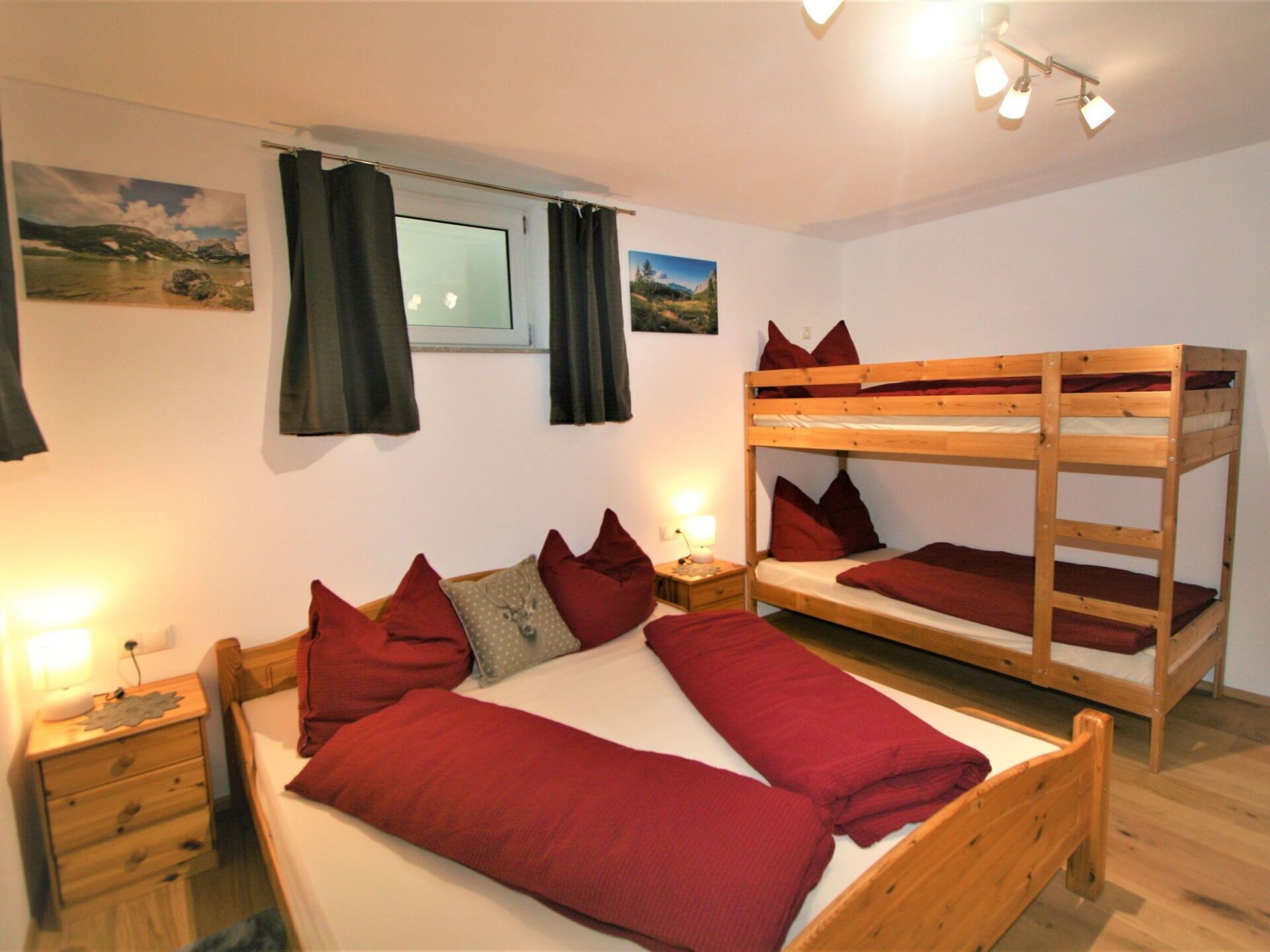 A room with a bunk bed, a single bed, a nightstand, a lamp, and a window with curtains.