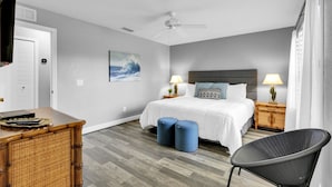A bedroom with a bed, two bedside tables, a chair, a television, and a ceiling fan.