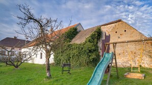 A grassy backyard with a slide, a tree, and a building with a sloped roof.