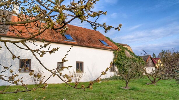 A traditional white building with a red-tiled roof, small windows, and a grassy lawn.