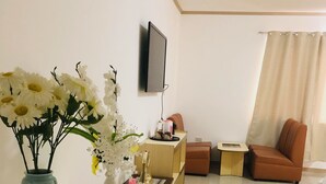 Un salon moderne avec un canapé blanc, un canapé marron, un téléviseur fixé au mur et un vase rempli de fleurs posé sur une table blanche.