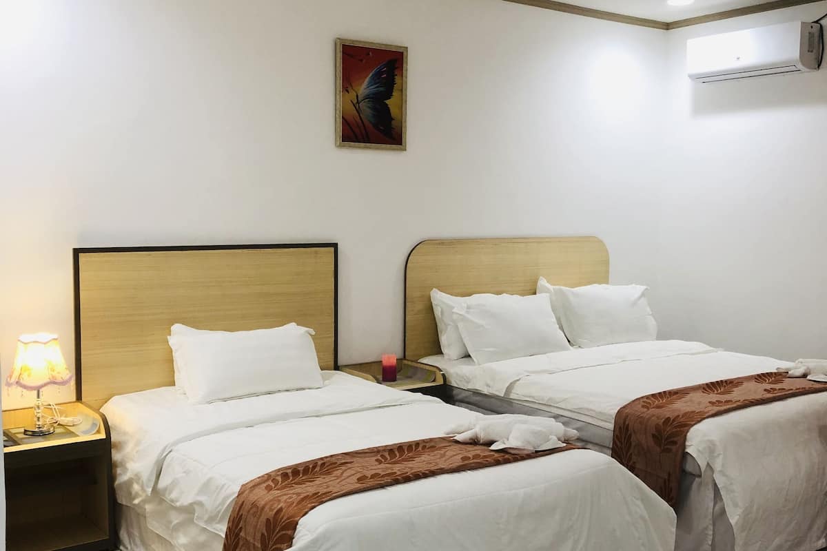 A hotel room with two beds, a nightstand with a lamp, a painting on the wall, and an air conditioning unit.