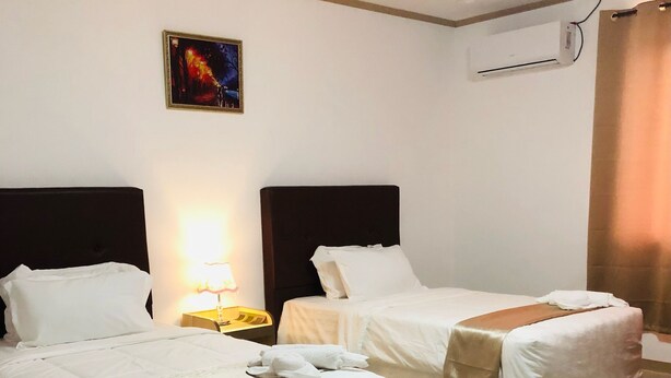 Habitación de hotel con dos camas, una mesita de noche, una lámpara, un equipo de aire acondicionado y un cuadro en la pared.
