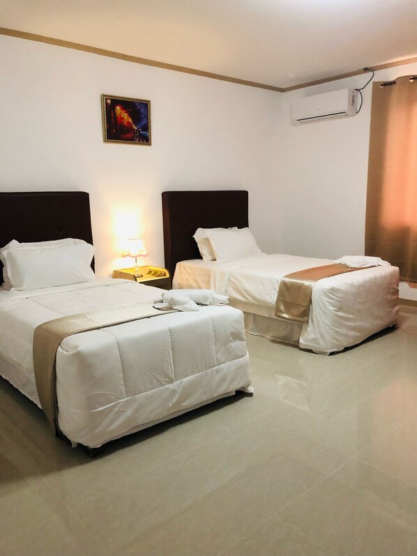 Habitación de hotel con dos camas, una mesita de noche, una lámpara, un equipo de aire acondicionado y un cuadro en la pared.
