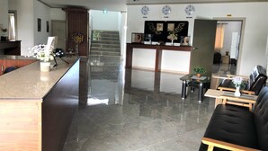 Un hall d’hôtel comprenant un comptoir d’accueil, un espace salon avec un canapé et des fauteuils, un escalier et des horloges indiquant l’heure de différentes villes.