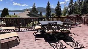 A deck with a table and chairs, overlooking a lake and mountains. - Mountain Harbor Cottage at Whitefish Lake #116 (Whitefish)