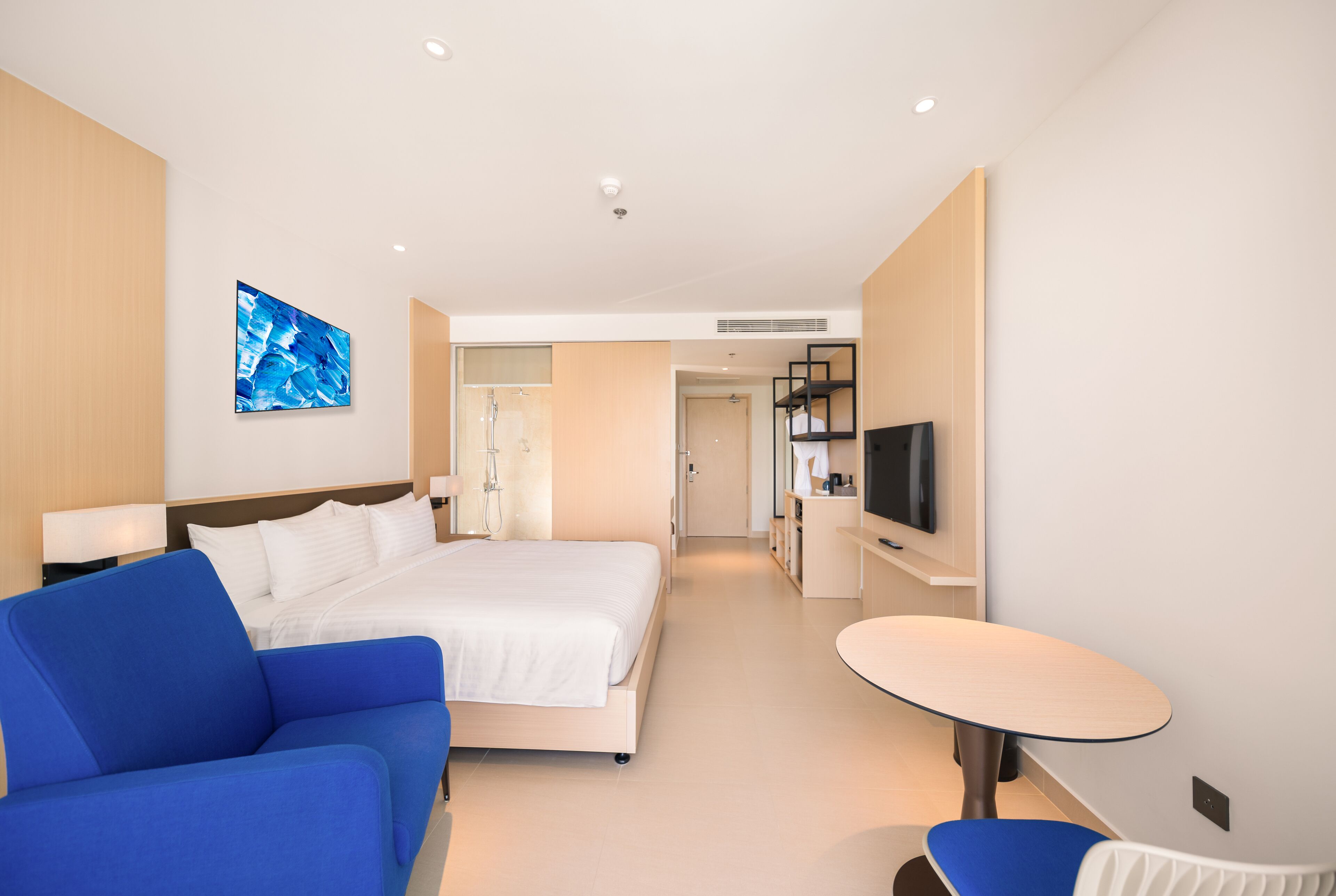 A modern hotel room with a large bed, a blue sofa, a small table, and a TV.