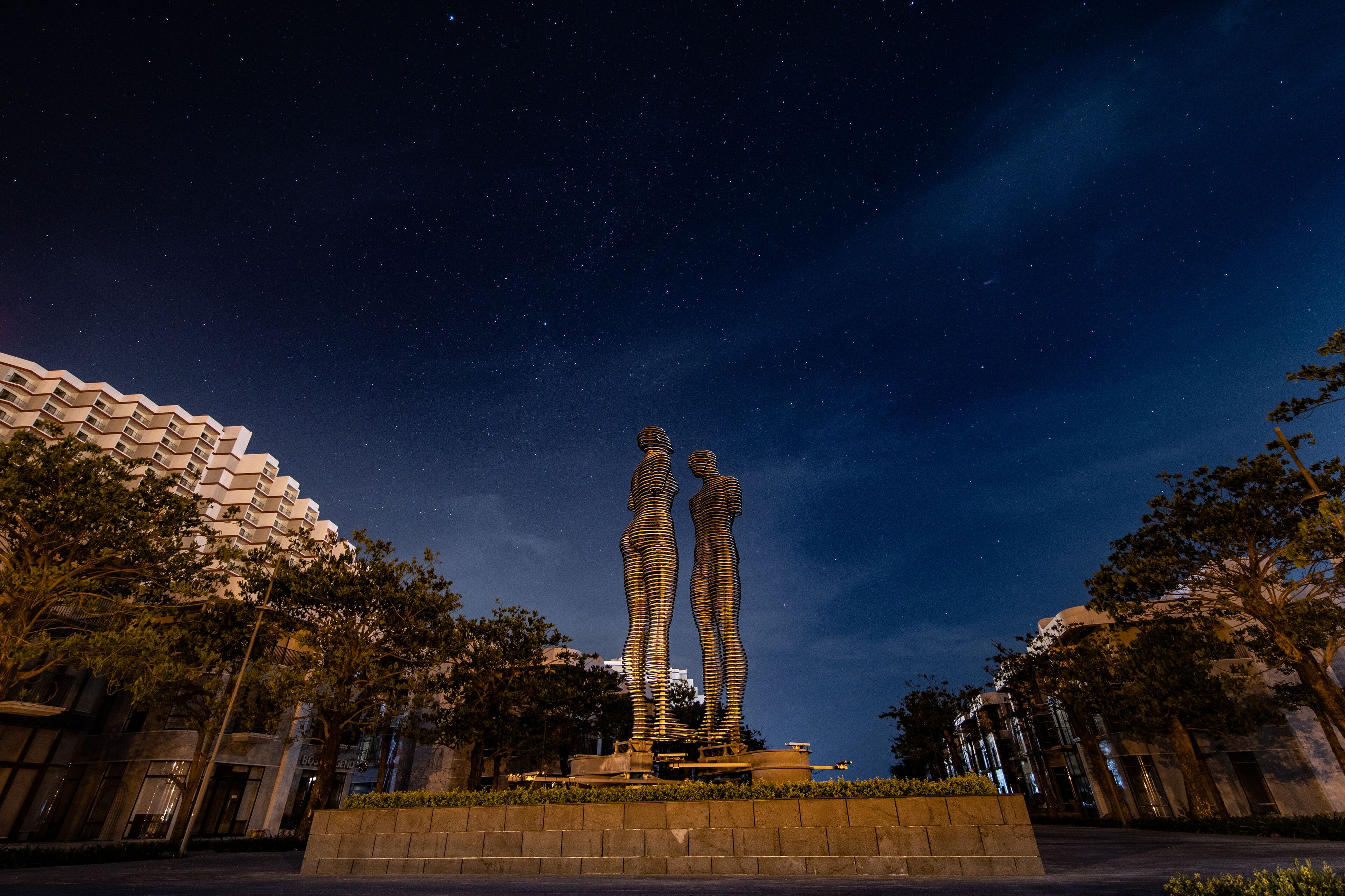Vista nocturna de un edificio moderno con un diseño arquitectónico único, que presenta dos esculturas altas y estilizadas en primer plano.