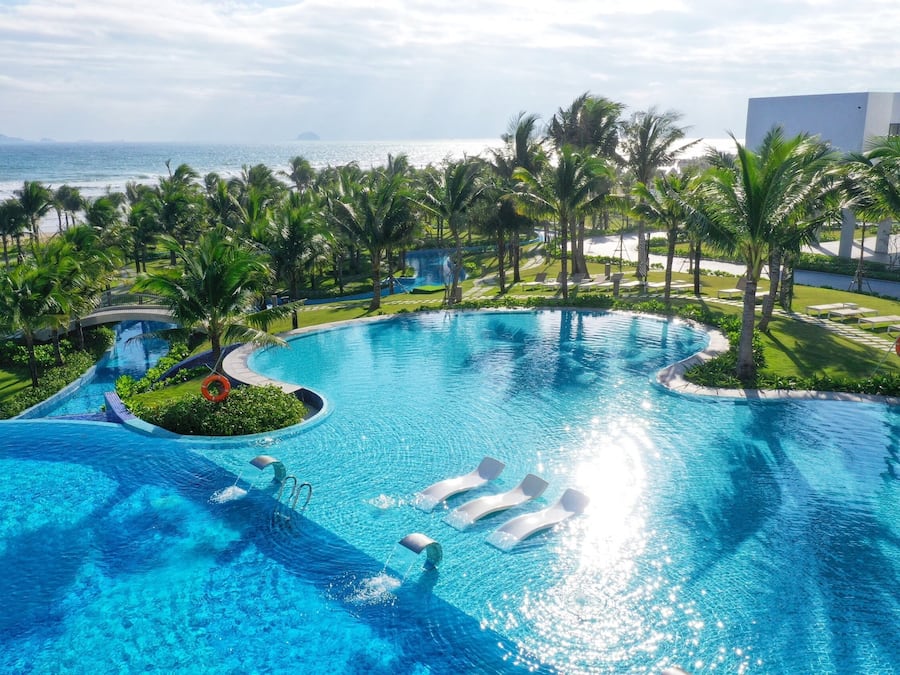 Une piscine d’un complexe hôtelier, avec une eau d’un bleu cristallin, entourée de palmiers et offrant une vue sur l’océan.