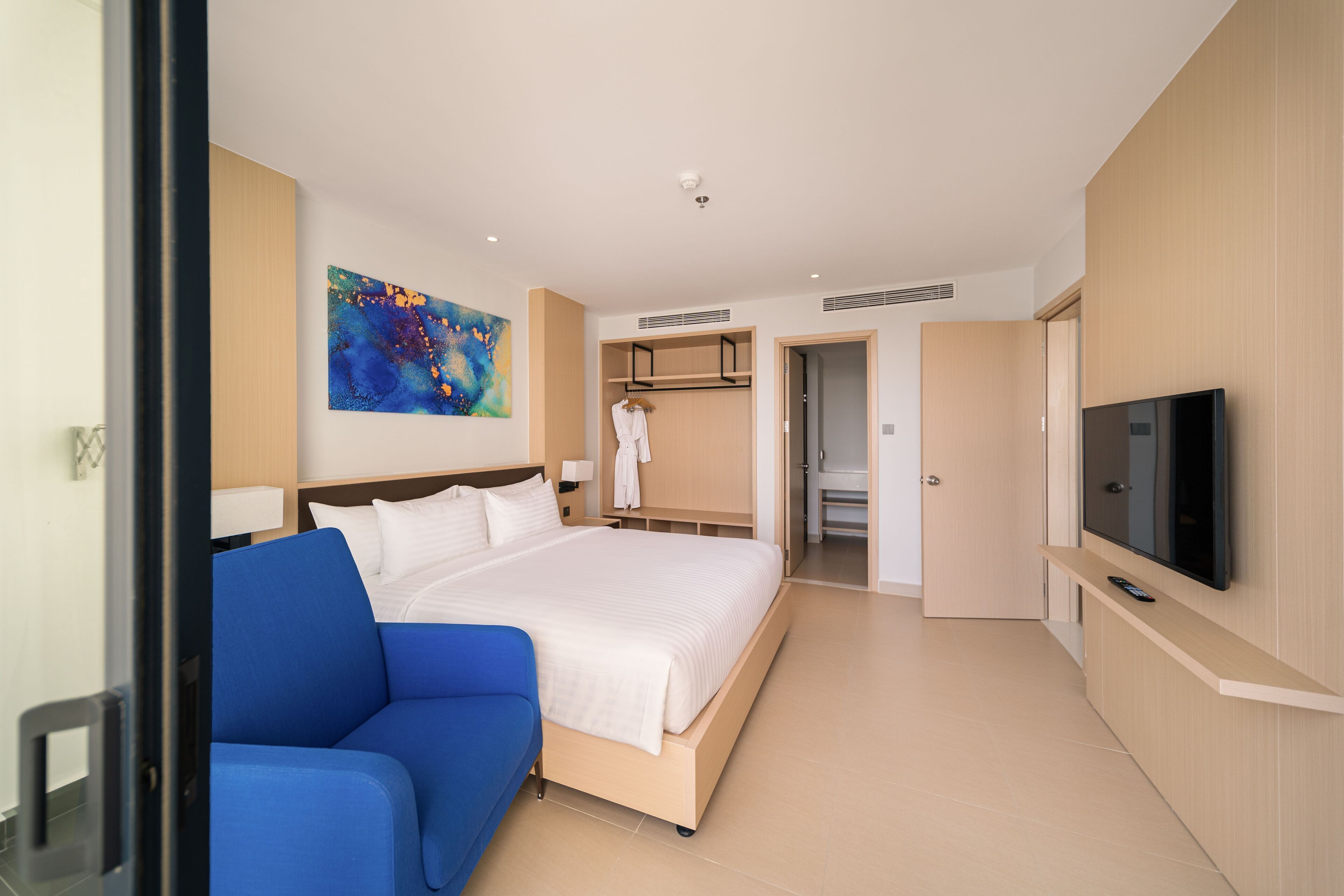 A modern hotel room with a large bed, a blue sofa, a TV, and a walk-in closet.