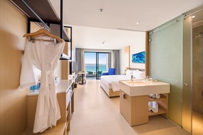 A modern hotel room with a large bed, a bathroom with a sink and mirror, a robe hanging on a rack, and a view of the sea through the window.
