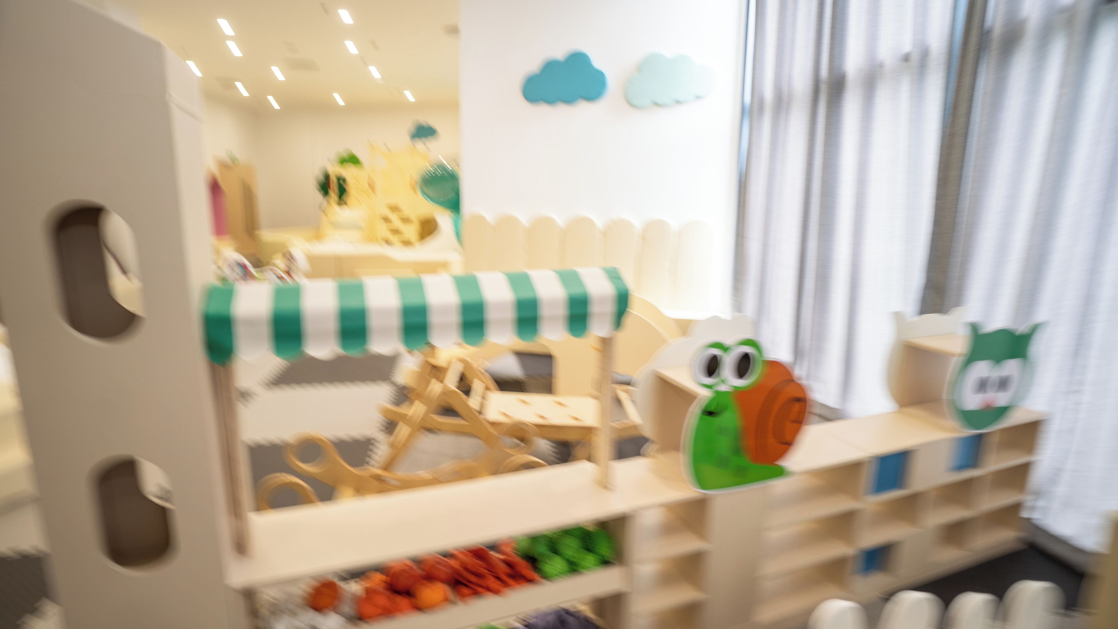 A children's play area with a green and white striped canopy, a wooden play structure, and a shelf with toys.