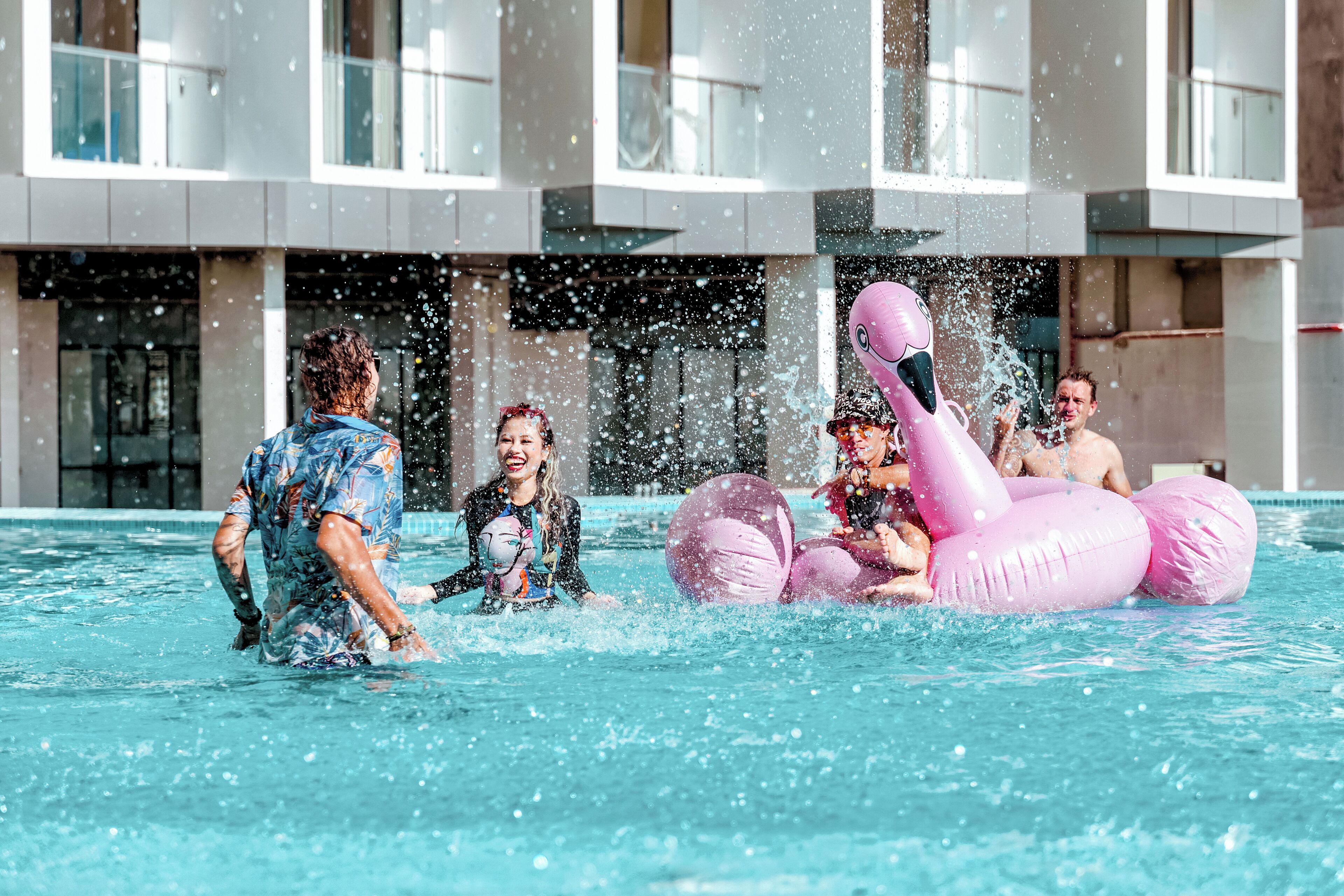 A swimming pool with people playing and a building in the background.
