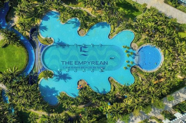 An aerial view of The Empyrean Cam Ranh Beach Resort with multiple swimming pools surrounded by palm trees.