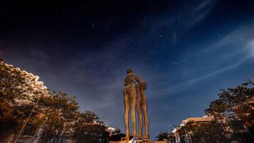 A night scene with a starry sky, a large sculpture of figures, and a person sitting in front of it.