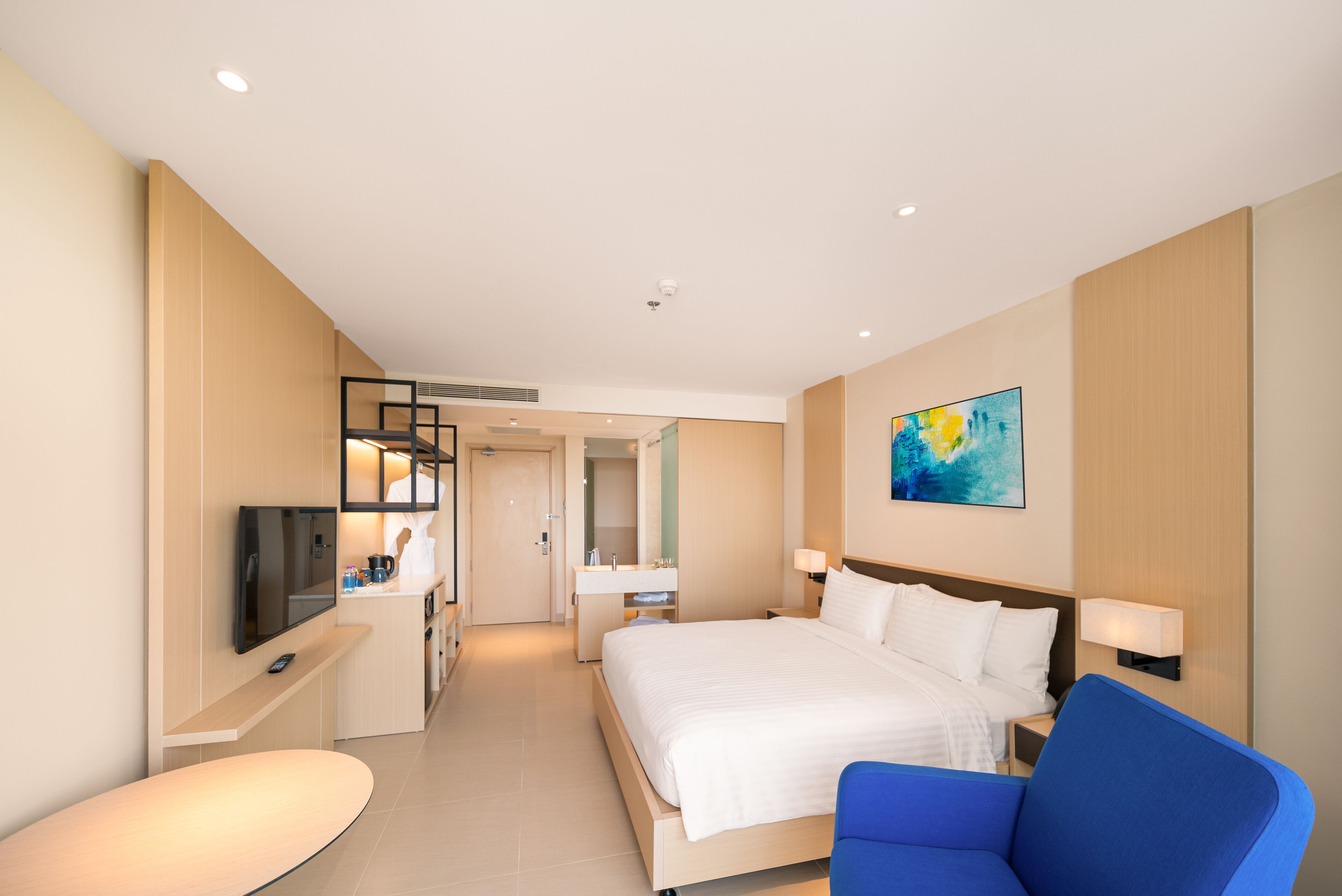 A modern hotel room with a large bed, a desk, a television, and a bathroom visible through an open door.
