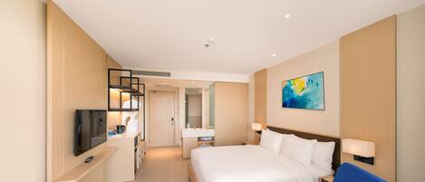 A modern hotel room with a large bed, a desk, a television, and a bathroom visible through an open door.