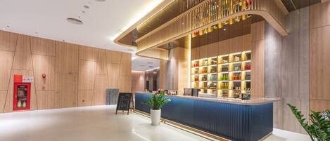 A modern reception area with a wooden reception desk, a digital screen, and a plant.