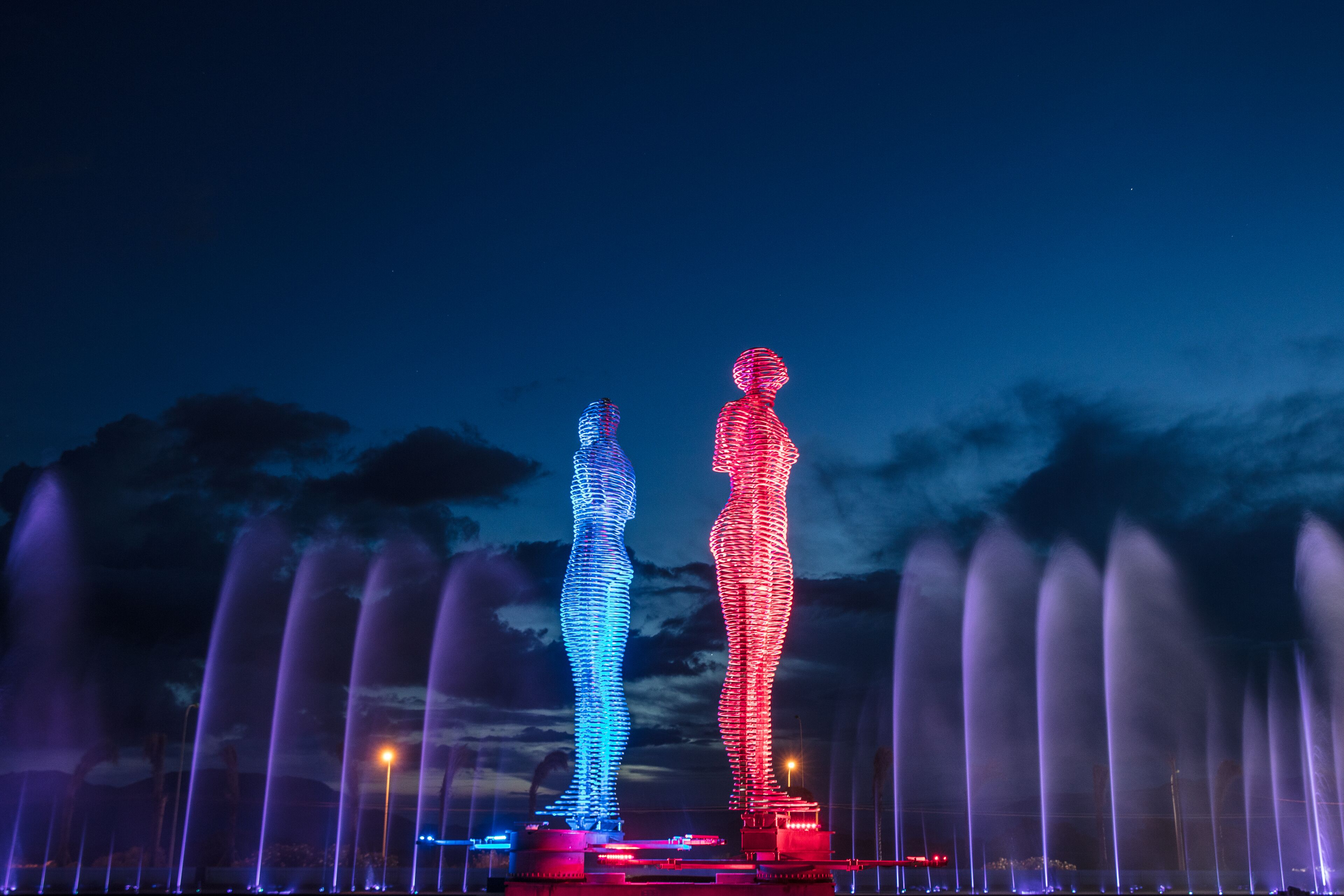 Une scène nocturne avec deux silhouettes illuminées et un jeu de fontaines.