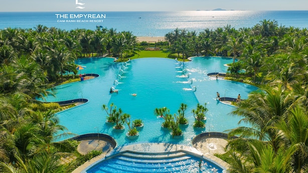 Una gran piscina infinita con múltiples carriles rodeada de palmeras, con vista a la playa y al océano.