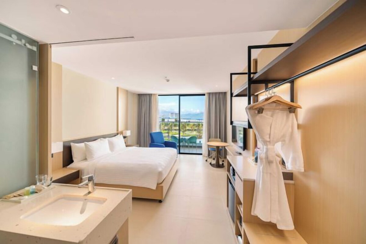 A modern hotel room with a large bed, a separate bathroom, a seating area with a view, and a robe hanging on the wall.