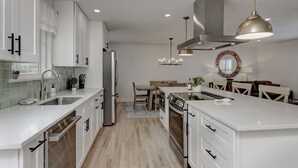 A modern kitchen with white cabinetry, a central island, and a dining area with wooden chairs and a table.