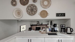 A modern kitchen with a central island, white cabinetry, and a coffee bar sign.