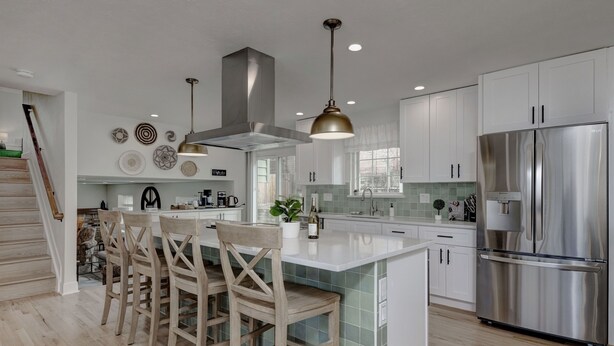 A modern kitchen with a central island, stainless steel appliances, and wooden chairs.