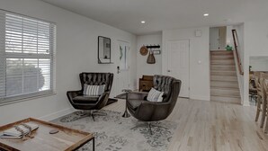 A spacious living room with two leather armchairs, a wooden coffee table, and a patterned rug. A staircase leads to a loft area with a wooden railing.