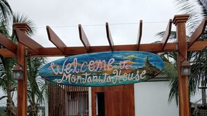 Una pérgola de madera con un letrero que dice "Welcome to Montanita House" sobre un conjunto de escaleras que conducen a un edificio blanco.
