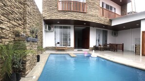 Una piscina con terraza de madera, pared de piedra y balcón con barandillas de madera.