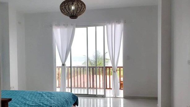 Un dormitorio con cama, un ventanal con cortinas, un balcón y una lámpara colgante.