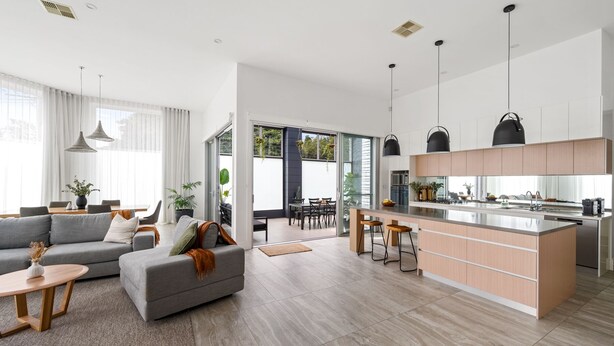Una cocina moderna con una isla central, un comedor con sofá y sillas, y una sala de estar con un ventanal grande.