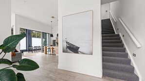 Un interior moderno con una escalera, una zona de comedor y un cuadro grande en la pared.