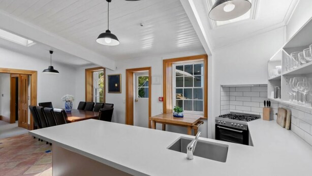 A modern kitchen with a large island, a dining area with a wooden table, and a kitchen island with a sink. - Historic Stone Cottage Apt 1- spa - 3 min from town (Queenstown)