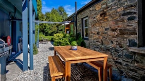 A wooden table with a bench in a garden area with a stone building and a blue structure in the background. - Historic Stone Cottage Apt 1- spa - 3 min from town (Queenstown)